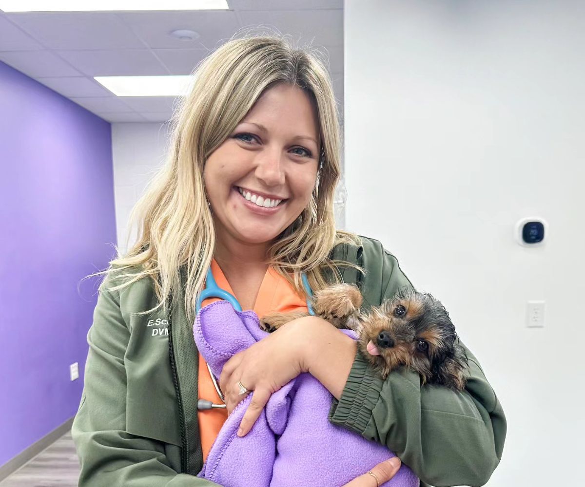 A vet staff smiling and holding a dog