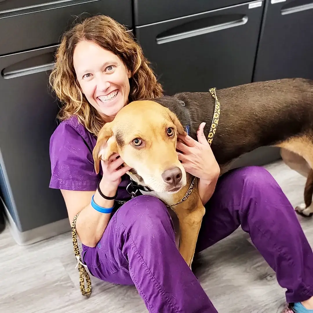 STATVet-Team-08 Veterinary technician sitting on the floor, smiling, and hugging a large dog.